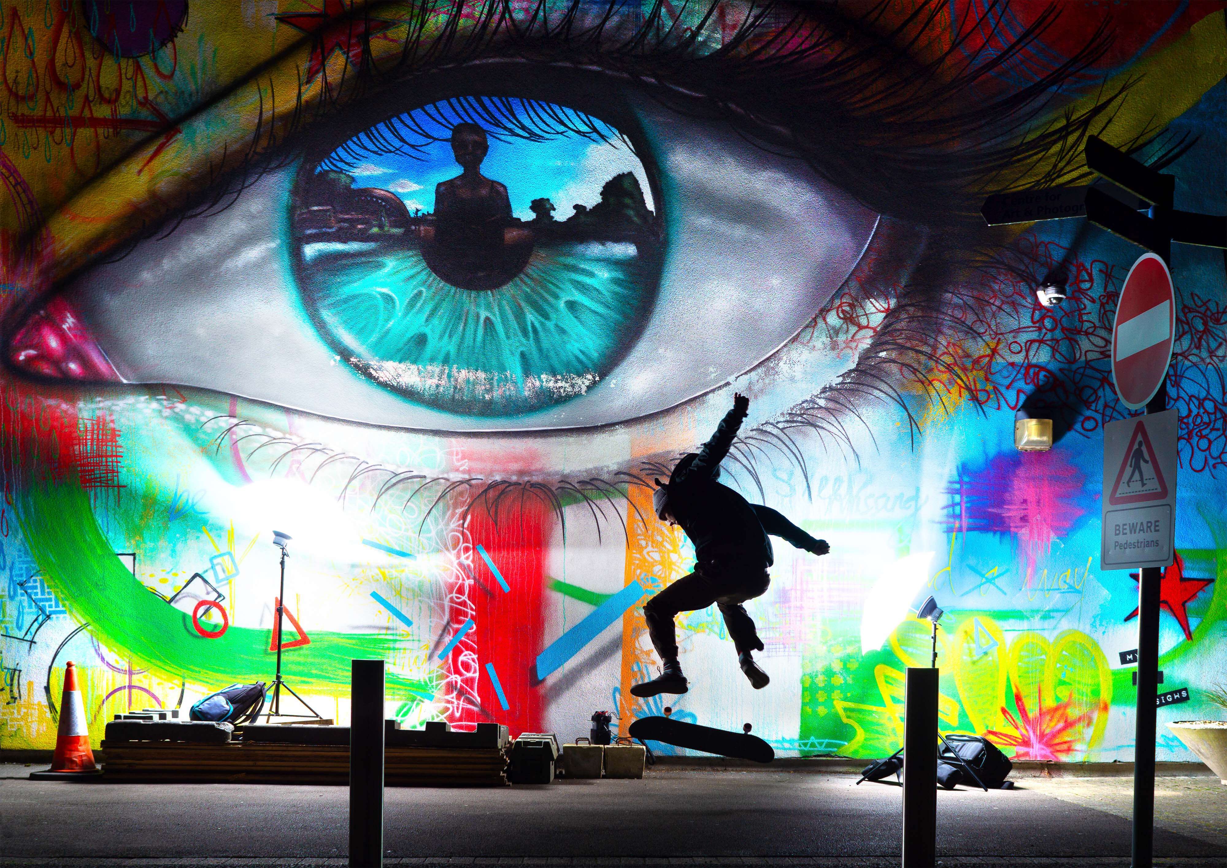 A silhouette image of skateboarder in action in front of colourful mural.